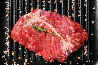 Izgara tavada üst bıçak bifteği, çiğ et, mermer sığır eti. Siyah arka plan. Üst görünüm.