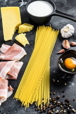 Geleneksel İtalyan alla carbonara makarna malzemeleri. Pişmemiş spagetti, pancetta pastırması, parmesan peyniri, yumurta. Siyah arka plan. Üst görünüm.