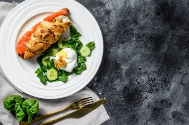Taze salata yapraklı, ıspanaklı, yumurtalı ve sebzeli tuzlu somonlu kruvasan sandviçi. Siyah arka plan. Üst Manzara. Boşluğu kopyala.