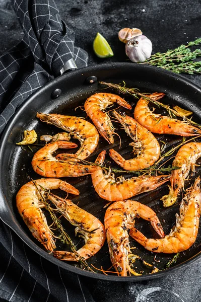 Grilled giant prawns, shrimps with garlic, lemon, spices in pan. Black background. Top view.