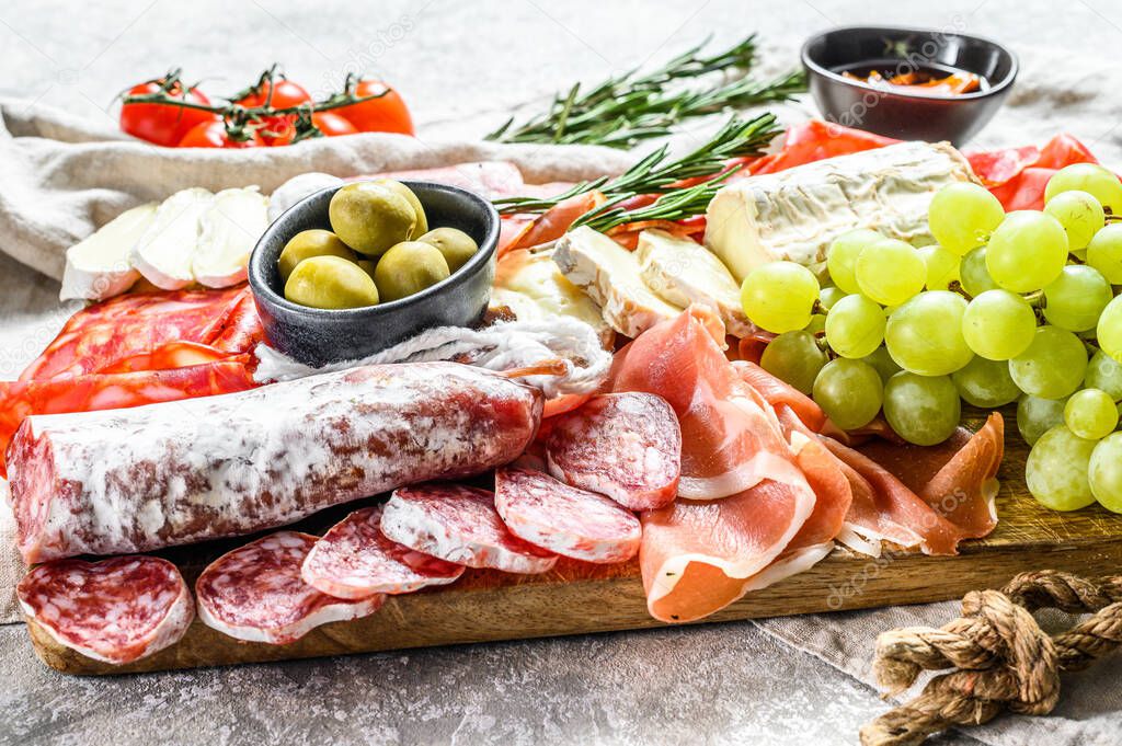 Italian antipasto, wooden cutting board with prosciutto, ham, parma, goat and Camembert cheese, olives, grapes. antipasti. Gray background. Top view.