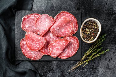 Salamlı sosis dilimleri siyah bir doğrama tahtasında. Karanlık arka plan. Üst görünüm.