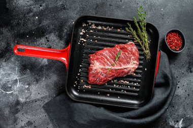 Izgara tavada üst bıçak bifteği, çiğ et, mermer sığır eti. Siyah arka plan. Üst görünüm.