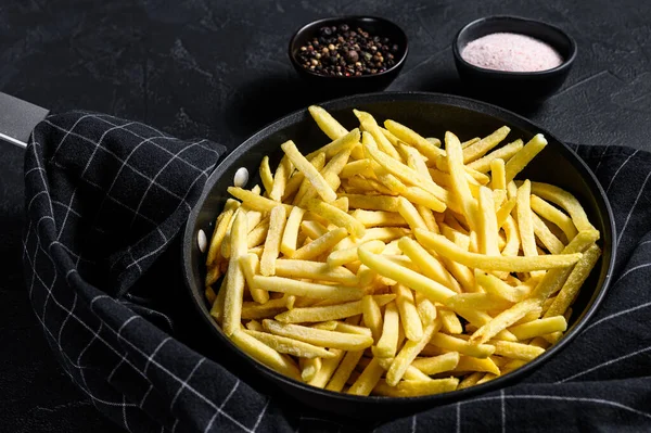 Frozen French fries in a frying pan. Black background. Top view.