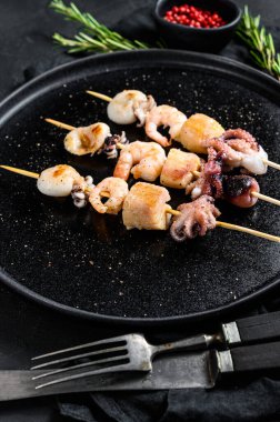 Karides, ahtapot, mürekkep balığı ve midyeli tahta şişler. Deniz mahsullü kebap. Siyah arka plan. Üst görünüm.