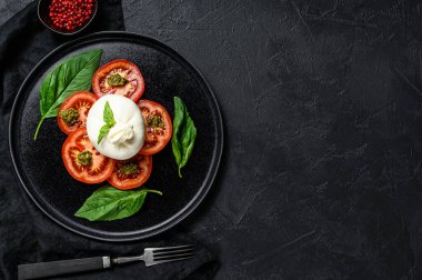 Siyah tabakta servis edilen Burrata peyniri ve domates salatası. Karanlık arka plan. Üst Manzara. Metin için boşluk.