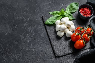 Mini mozzarella peyniri, fesleğen yaprağı ve vişneli domates, Caprese salatası. Siyah arka plan. Üst Manzara. Boşluğu kopyala.