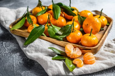 Ahşap bir kasede yaprakları olan taze mandalina ve portakal. Gri arka plan. Üst görünüm.