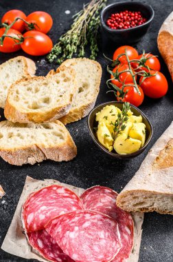 Bagetli sandviç malzemeleri - jambon, salam, peynir, tereyağı, domates. Siyah arka plan. en üstteki görünüm.