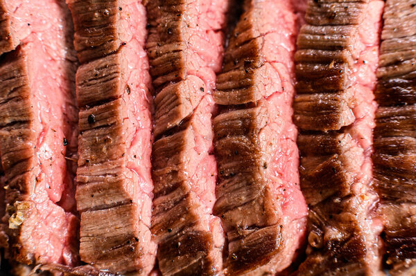 Roasted medium rare sliced flank beef steak. Black background. Top view.