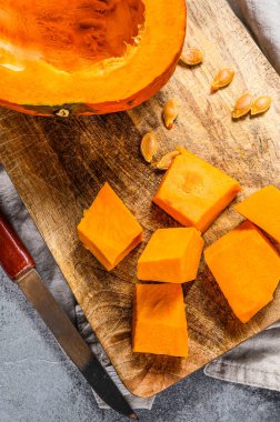 Kesme tahtasındaki çiğ balkabağı, küp şeklinde kesilmiş. Gri arka plan. Vejetaryen mutfağı.