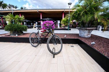 Çiçeklerin arasında bir alışveriş merkezinde park etmiş bisiklet. 07.01.2020 Tenerife, Kanarya Adaları.