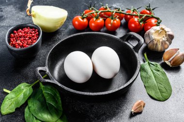 Kızarmış ya da haşlanmış yumurta ile kahvaltı hazırlama kavramı. Yumurta, soğan, sarımsak, domates, biber, ıspanak. Siyah arka plan. Üst görünüm.