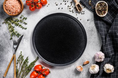 Taze çiğ sebze ve sebzelerin ortasında siyah boş bir tabak. Sağlıklı, temiz yemek, vejetaryen, diyet yemek konsepti. Beyaz arka plan. Üst Manzara. Boşluğu kopyala