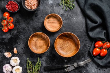 Taze çiğ yeşilliklerin ve sebzelerin ortasında siyah boş ahşap tabaklar. Sağlıklı, temiz yemek, vejetaryen, diyet yemek konsepti. Siyah arka plan. Üst Manzara. Boşluğu kopyala