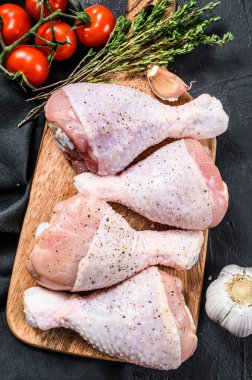 Tahta bir tahtanın üzerinde baharatlı ve sebzeli çiğ tavuk bacağı. Siyah arka plan. Üst görünüm.