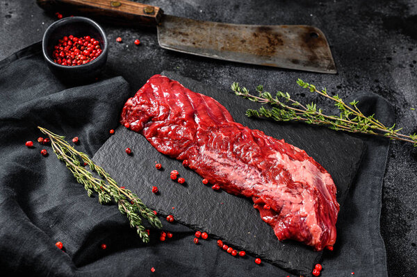 Raw marbled beef steak with pink pepper and thyme. Black background. Top view.