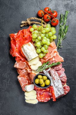 İtalyan antipasto, jambon, parma, keçi peyniri, zeytin ve üzümlü ahşap kesim tahtası. Antipasti. Siyah arka plan. Üst görünüm.