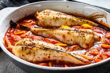 Fırın kabında domateslerde pişirilmiş maymunbalığı. Siyah arka plan. Üst görünüm.