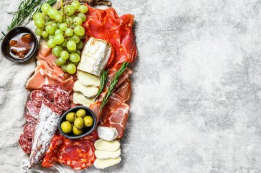 Üzümlü soğuk et, prosciutto, jambon, kurutulmuş et, sucuklu salam, fuet, camembert ve keçi peyniri. Gri arka plan. Üst Manzara. Boşluğu kopyala.