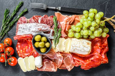 Üzümlü soğuk et, prosciutto, jambon, kurutulmuş et, sucuklu salam, fuet, camembert ve keçi peyniri. Siyah arka plan. Üst görünüm.