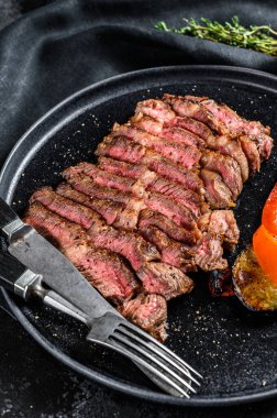 Dilimlenmiş sığır eti, az pişmiş biftek. Yanında sebze tabağı olan bir tabakta yuvarlan. Siyah arka plan. Üst görünüm.