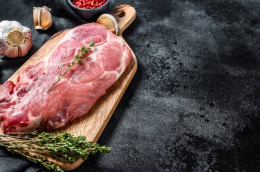 Çiğ domuz pirzolası. Bir parça çiğ et, yeşillik ve baharatla hazırlanmaya hazır. Siyah arka plan. Üst Manzara. Boşluğu kopyala.