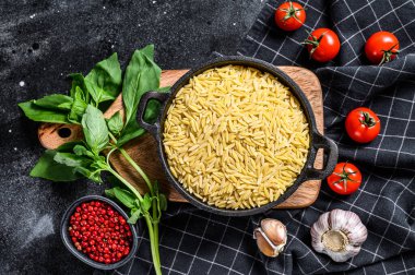 Bir kase pişmemiş, fesleğenli, domatesli ve sarımsaklı Orzo makarna. Siyah arka plan. Üst görünüm