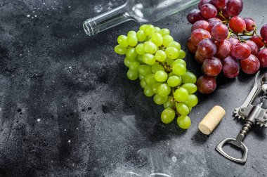 Bir dal yeşil ve kırmızı üzüm, bir şişe, bir tirbuşon ve bir mantar. Şarap yapma kavramı. Siyah arka plan. Üst Manzara. Boşluğu kopyala.