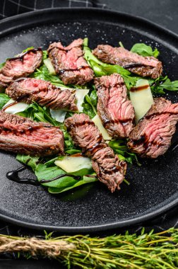 Ispanaklı biftek salatası, roka ve dilimlenmiş biftek. Siyah arka plan. Üst görünüm.