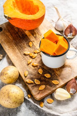 Kabak çorbası pişirme konsepti. Balkabağı parçaları, patates, sarımsak, kabak çekirdeği. Krema çorbası. Gri arka plan. Vejetaryen mutfağı.