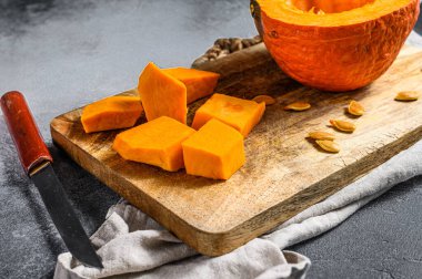 Kesme tahtasındaki çiğ balkabağı, küp şeklinde kesilmiş. Gri arka plan. Vejetaryen mutfağı.