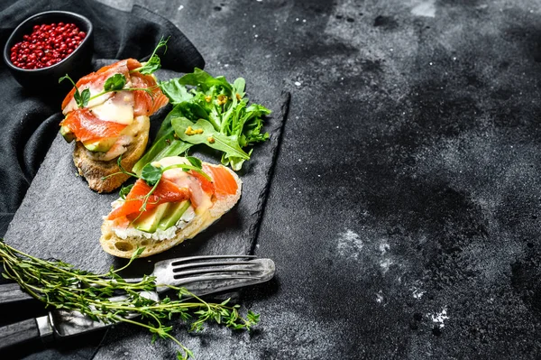 Toasts with avocado and smoked salmon. Black background. Top view. Copy space.