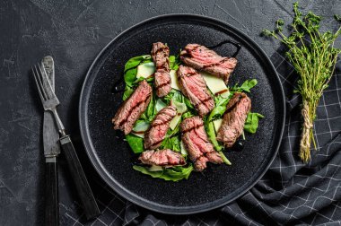 Ispanaklı biftek salatası, roka ve dilimlenmiş biftek. Siyah arka plan. Üst görünüm.