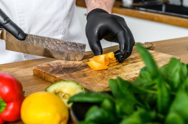 Siyah eldivenli bir şef odun kesme tahtasında domates doğruyor..