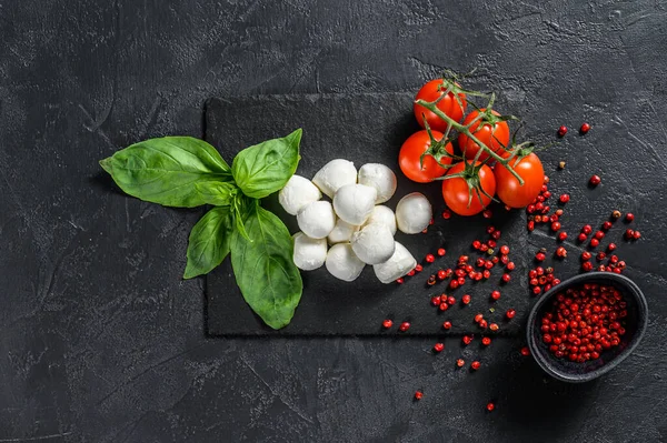 Caprese salatası, mini mozzarella peyniri, fesleğen yaprağı ve vişneli domates. Siyah arka plan. en üstteki görünüm.