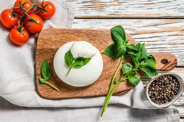 Italian Burrata buffalo cheese with Basil leaves. White wooden background. Top view.