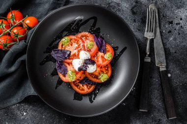 Caprese salatası. Kiraz domatesli, mozarella soslu ve mor fesleğenli sağlıklı bir yemek. Lezzetli ve sağlıklı bir vejetaryen yemeği konsepti. Siyah arka plan. en üstteki görünüm.