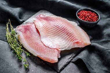 Kekik ve pembe biberli doğrama tahtasında çiğ telapia fileto. Siyah arka plan. Üst görünüm.