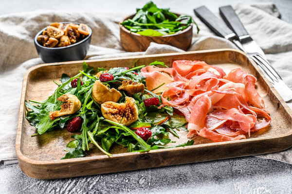 Salad with Parma, prosciutto ham, arugula and figs. Italian antipasti. Gray background, top view