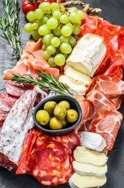 Üzümlü soğuk et, prosciutto, jambon, kurutulmuş et, sucuklu salam, fuet, camembert ve keçi peyniri. Siyah arka plan. Üst görünüm.