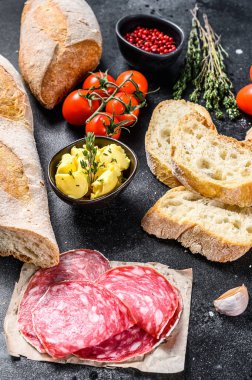 Tereyağlı sandviç, tütsülenmiş et, baget, vişneli domates, parmesan peyniri, sarımsak ve baharat. Siyah arka plan. en üstteki görünüm.