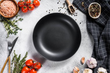 Taze çiğ sebze ve sebzelerin ortasında siyah boş bir tabak. Sağlıklı, temiz yemek, vejetaryen, diyet yemek konsepti. Beyaz arka plan. Üst Manzara. Boşluğu kopyala.