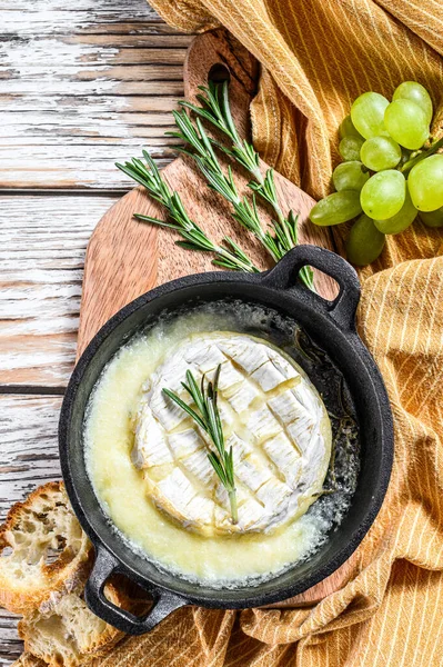 Baked brie cheese, Camembert with rosemary in a pan. White wooden background. Top view.