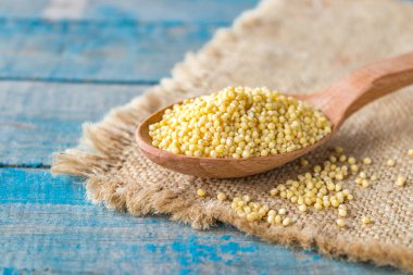 Çiğ sarı darı ahşap bir kaşıkta çuval bezi üzerinde mavi köy tahtalarının arka planında.