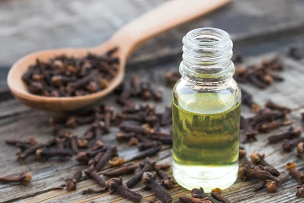 Una botella de aceite esencial de clavo se encuentra cerca de una cuchara con especias de clavo en tablas de madera viejas . — Foto de Stock