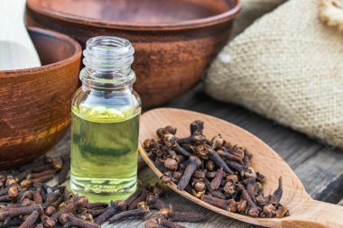 Bir şişe karanfil esaslı yağ eski ahşap tahtalarda karanfil baharatlarıyla bir kaşığın yanında duruyor..