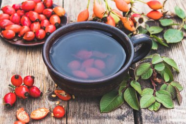 Tentür ya da kırmızı gül kalçalı çay, cam bir fincanda, tahta bir masanın üzerindeki gül kalçalarının yanında..