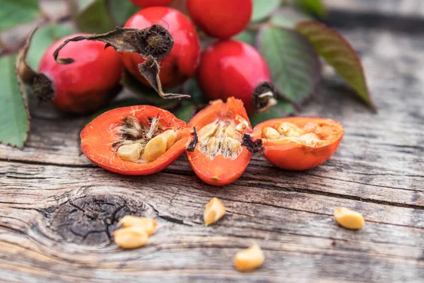 新鮮な赤いバラの腰と木のテーブルの上に種を半分に熟した果実. — ストック写真