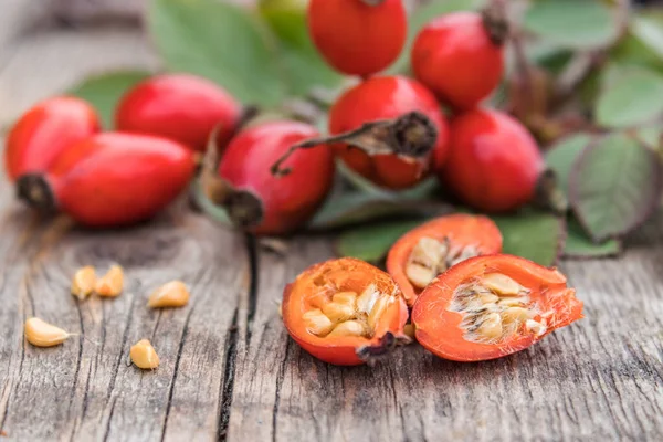 赤いバラの腰と熟した果実の半分に種子で古い木の板. — ストック写真